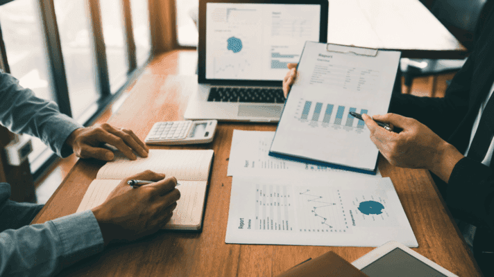 Business professionals analysing financial data and reports on a laptop and paper during a meeting