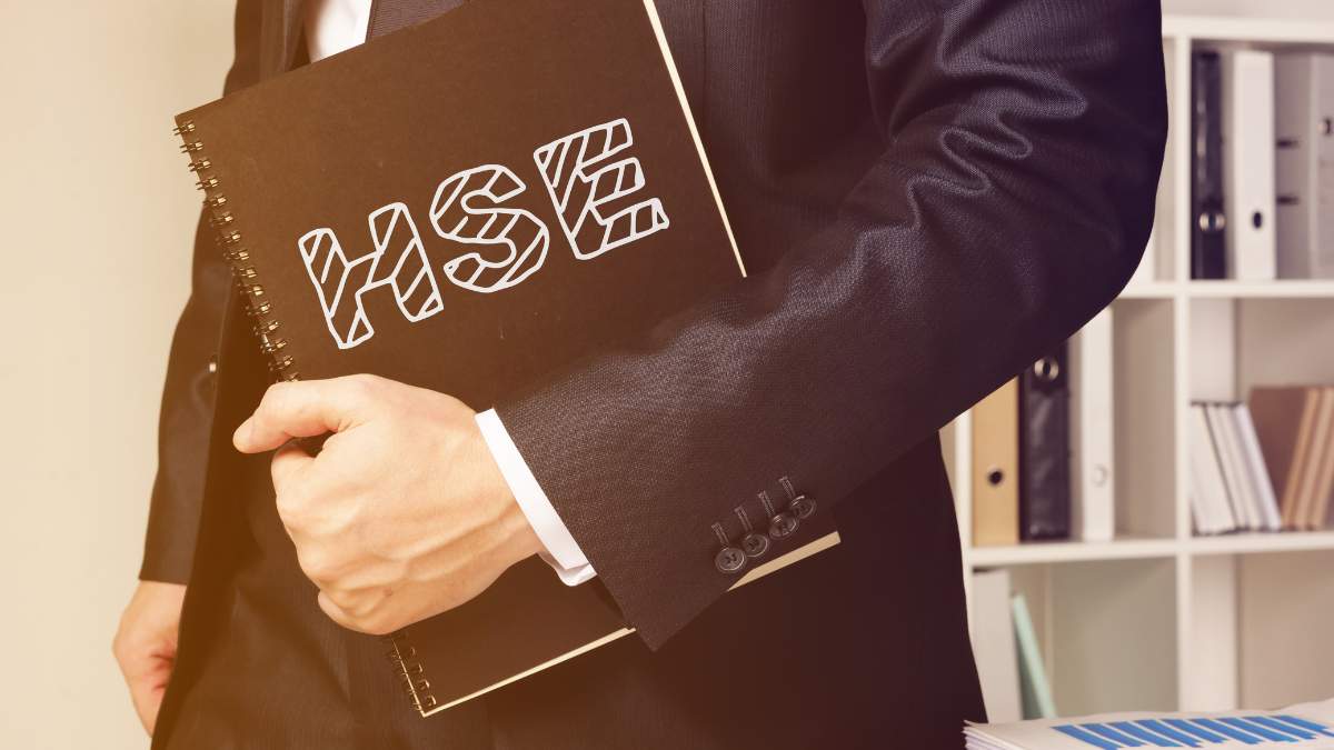 a person in a business suit is holding a black notebook with HSE in a creative font on its cover