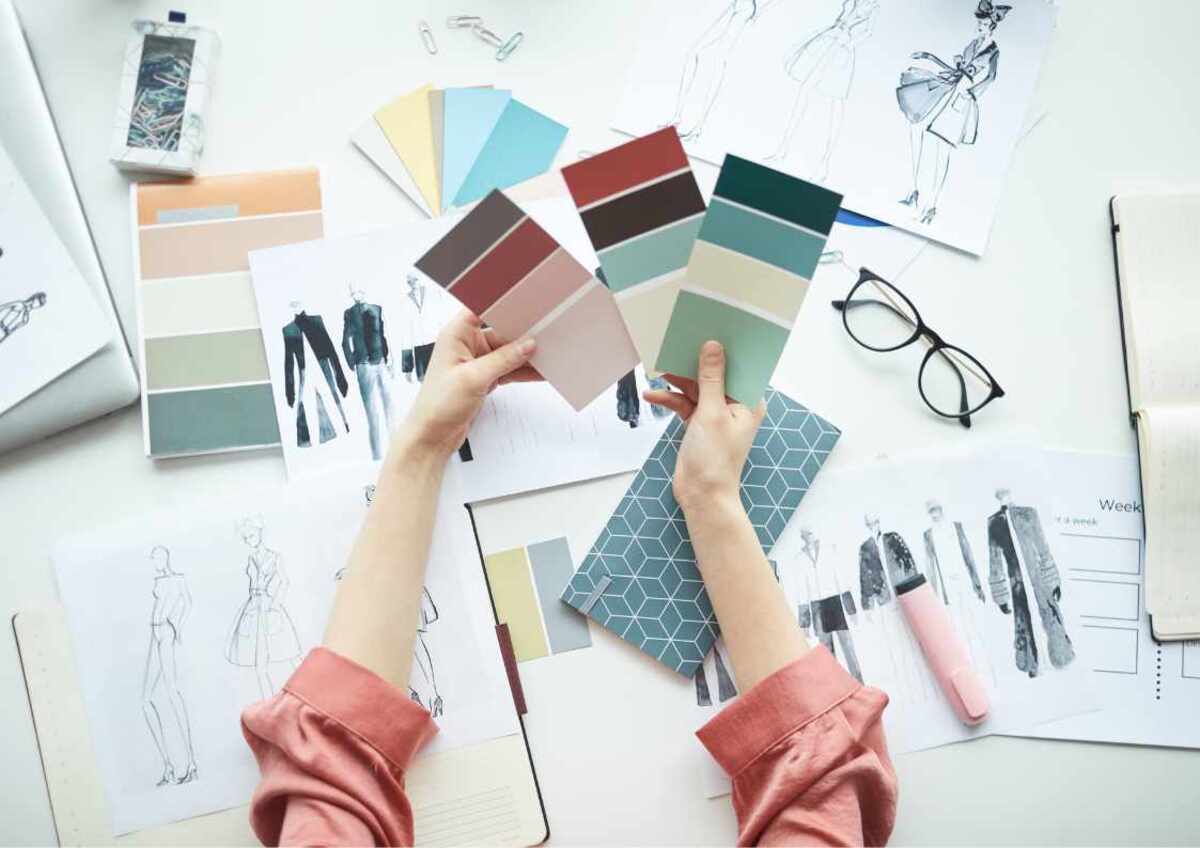 A person examining fashion design materials with colour palettes and sketches.