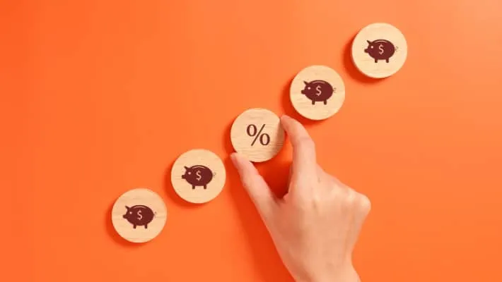 Hand arranging wooden coins with piggy and percentage symbols on orange background