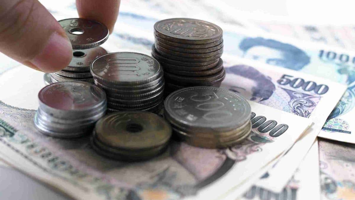 A person arranging Japanese coins beneath Japanese banknotes