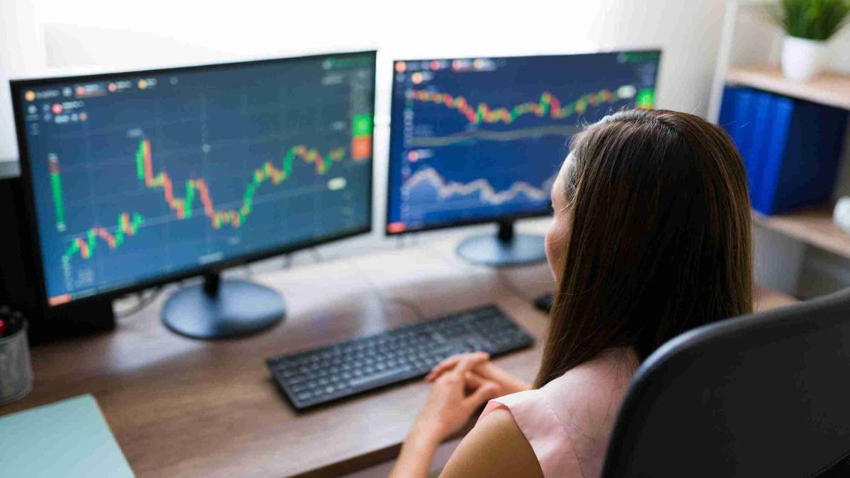 A woman concentrating on multiple screens, each displaying trading charts