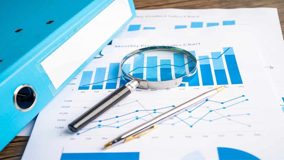 Magnifying glass over a bar chart with a pen pencil and binder on a wooden surface