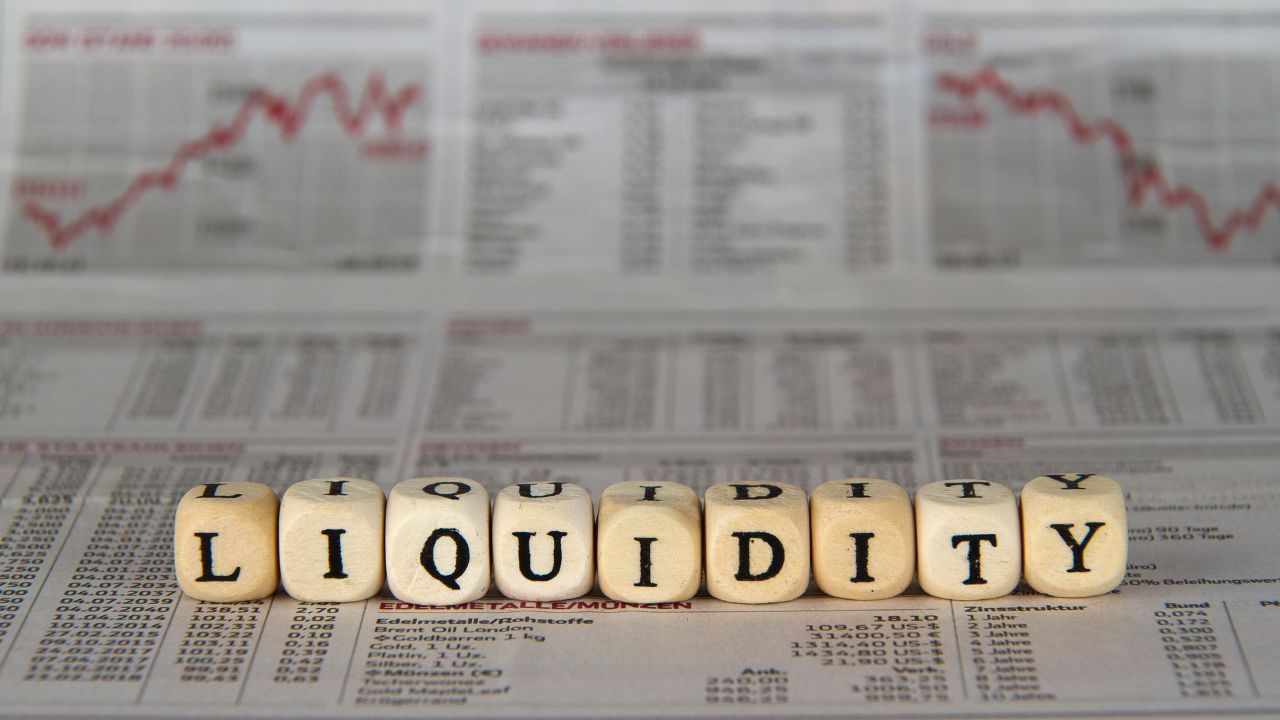 Blocks spelling LIQUIDITY in front of a financial newspaper