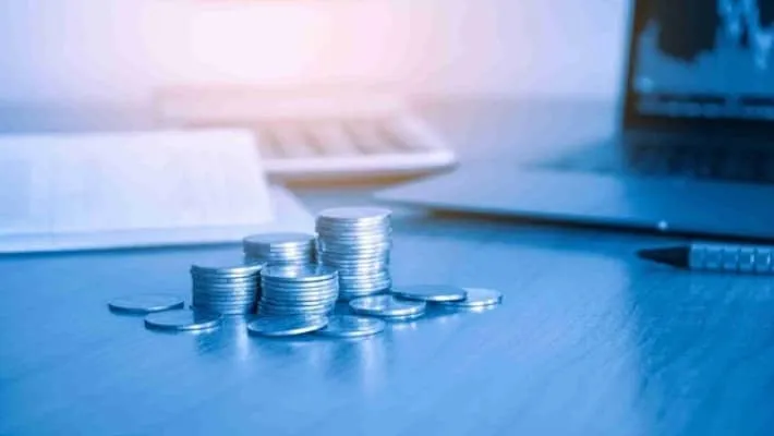 a stack of money coins with blurred calculator and laptop in the background