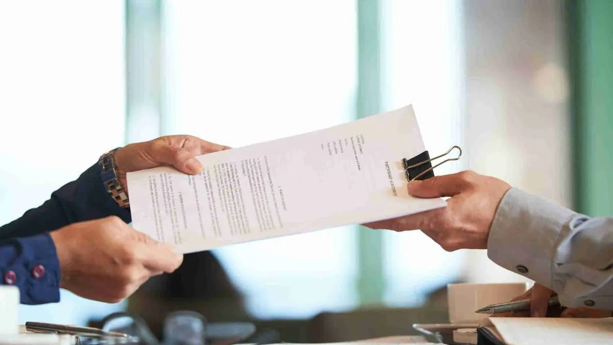 Close-up view capturing hands exchanging paperwork between two individuals