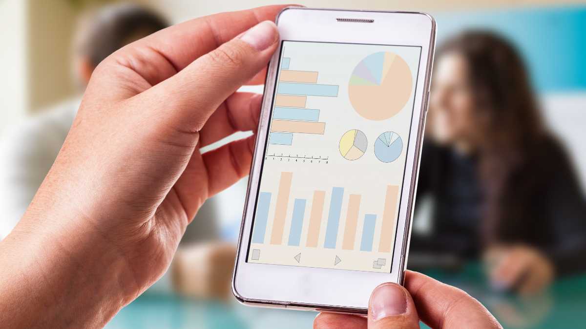 Hand holding a smartphone displaying graphs and charts