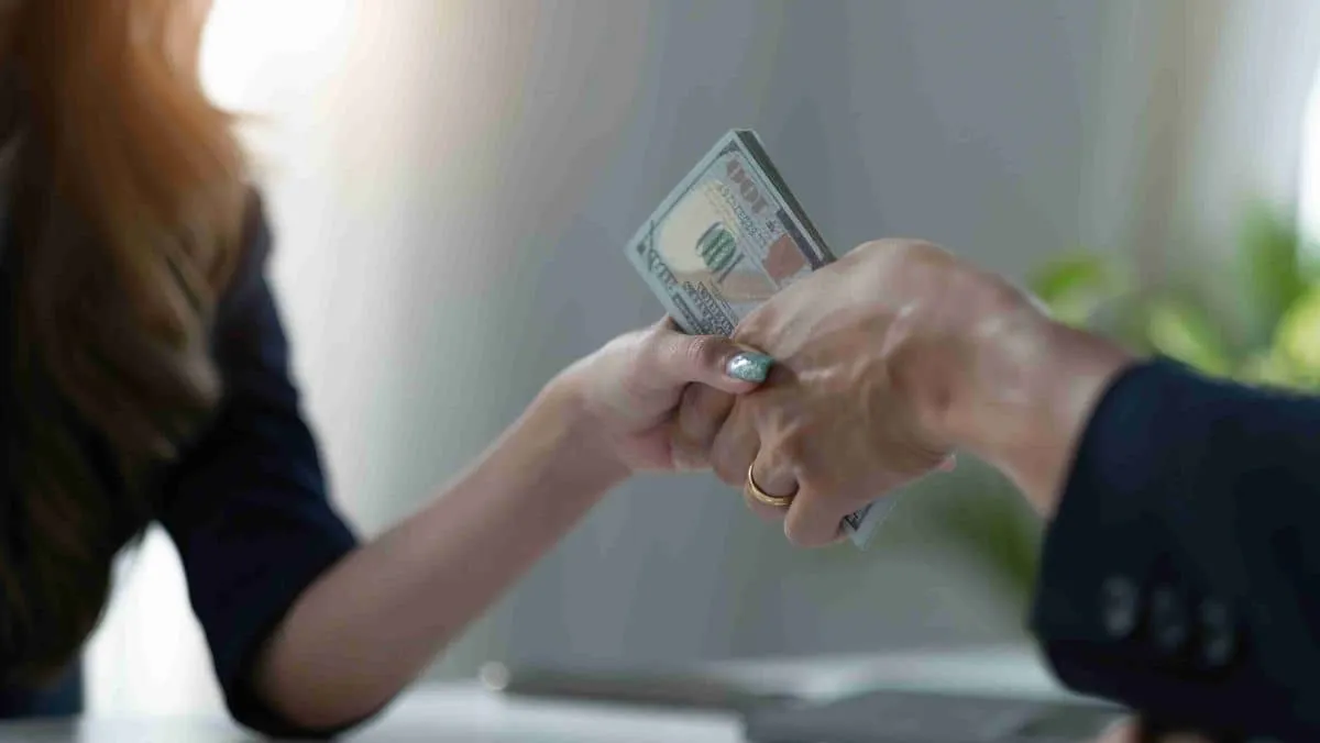 Handshake between two persons, with currency bills exchanged between their hands