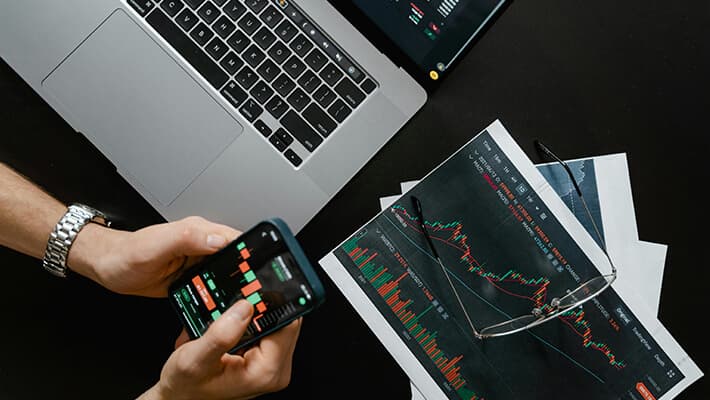 A man trading in mobile with printed stock chart and laptop