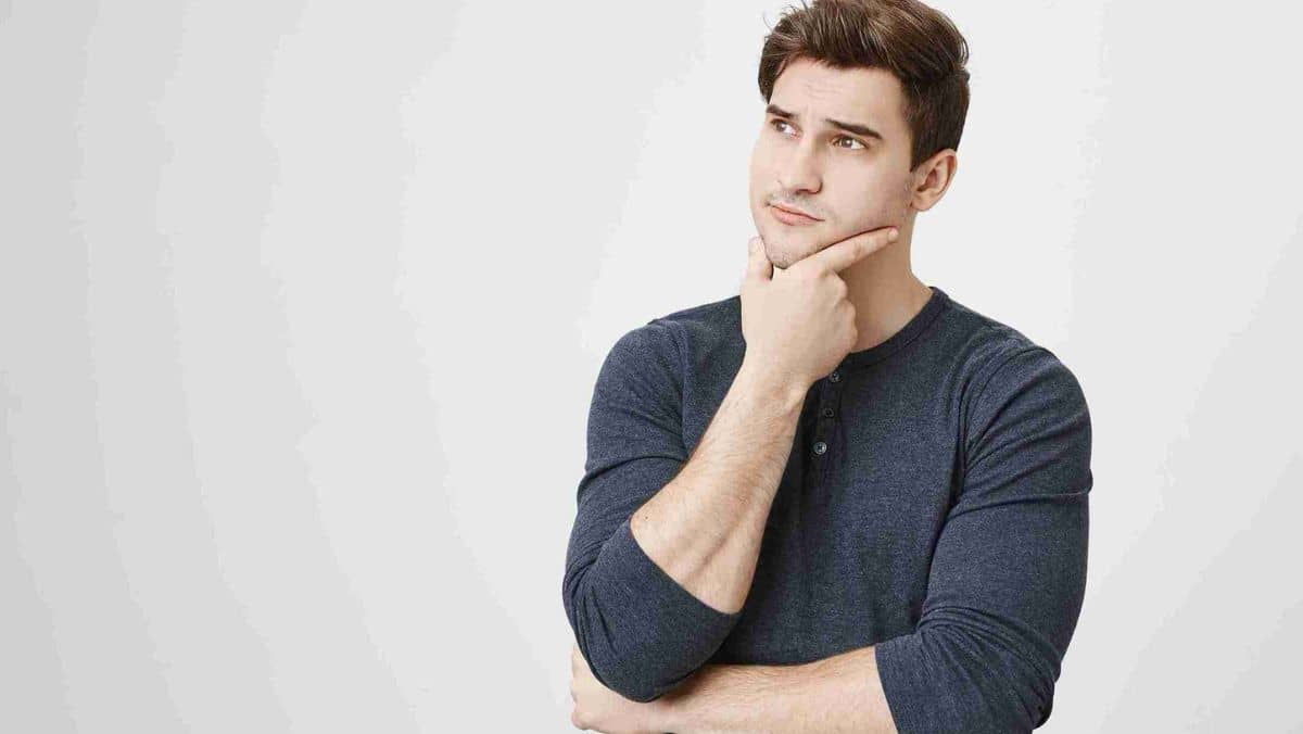 Man in a plain shirt deep in thought, holding his chin contemplatively