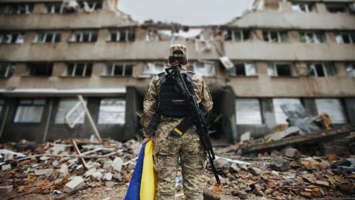 a soldier with a Ukraine flag in front of a ruined building