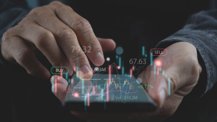 A hand indicating towards a trading chart hologram above an open laptop