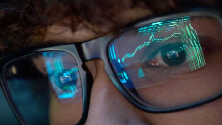 Young trader looking at trading charts reflecting in glasses, close up