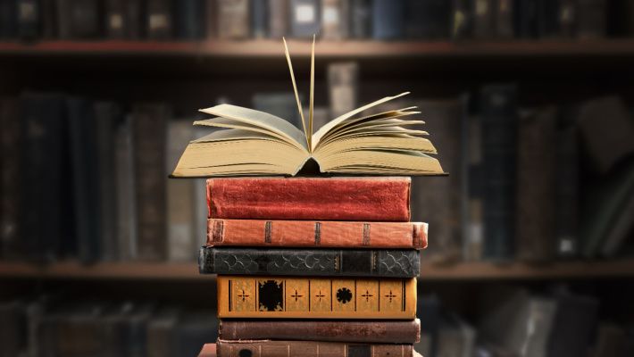 Several books stacked together with an shelves background