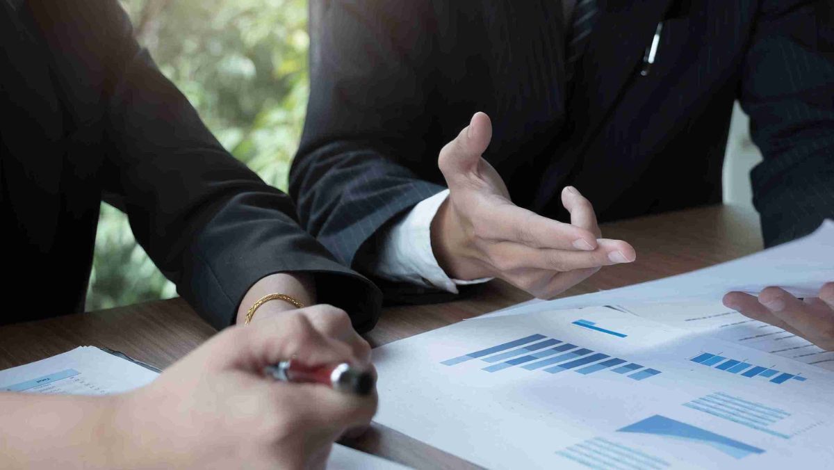 Two people talking with financial papers and graphs on the table