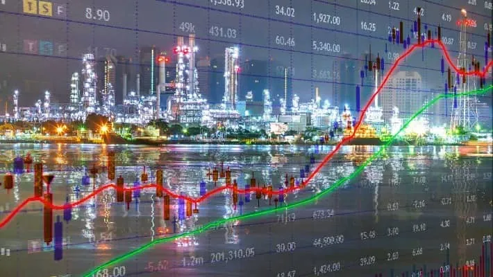 Overlay of stock market graphs on an industrial plant's night scene, indicating economic activity in the energy sector