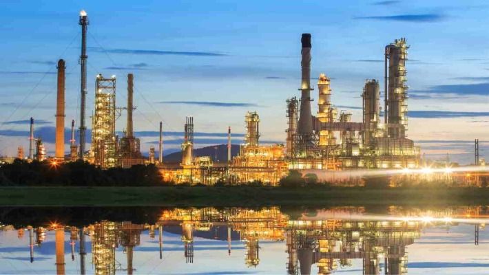 Oil refinery at dusk with lights reflected in water, showcasing industrial beauty