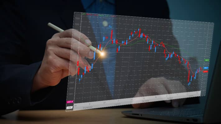 A trader pointing at financial charts on computer screens