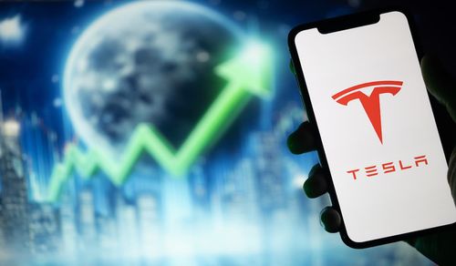 Hand holding mobile with Tesla logo and upward stock arrow, reflecting Tesla Model Y price increase.