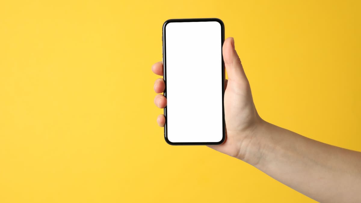 A hand holding a smartphone with a blank screen on a yellow background.